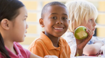 Kindergarten children eating lunch smiling at camera